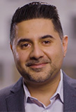 Portrait of Dr. Suleman Bhana taken from the shoulders up wear a gray suit jacket and light button up shirt