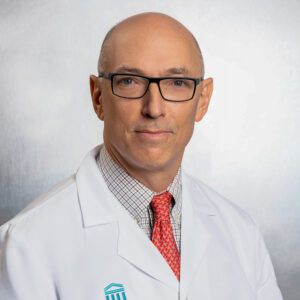 Headshot of Daniel Solomon wearing a lab coat, orange necktie and black glasses